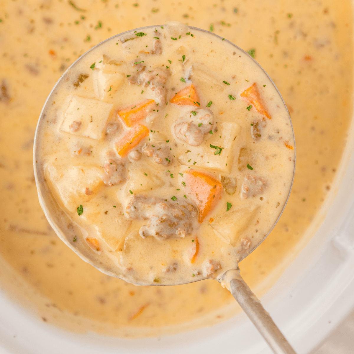 a close up of cheeseburger soup with potatoes, ground beef, and carrots in a ladle