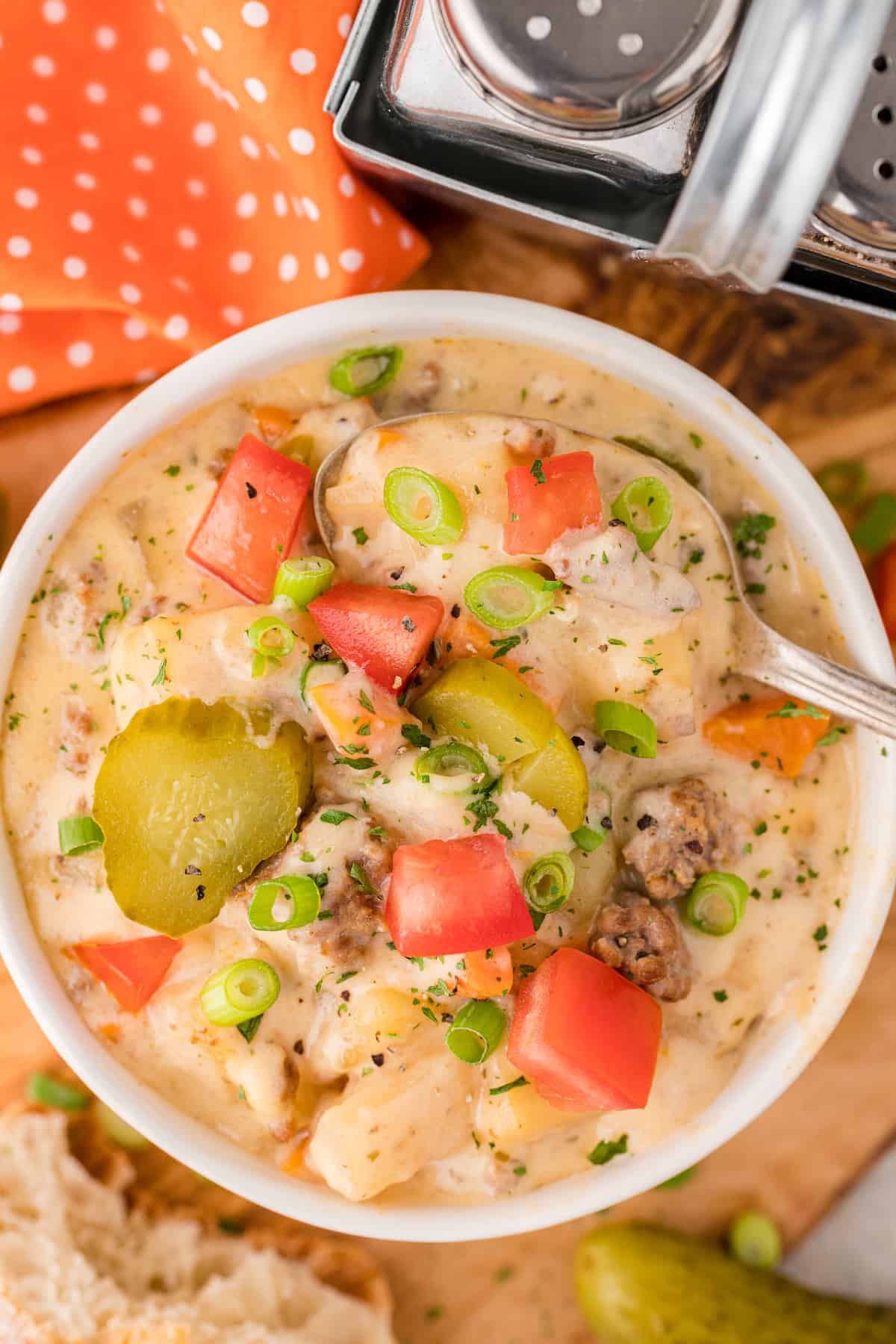 a close up of cheeseburger soup fresh out of the crockpot, garnished with pickles and chopped tomatoes