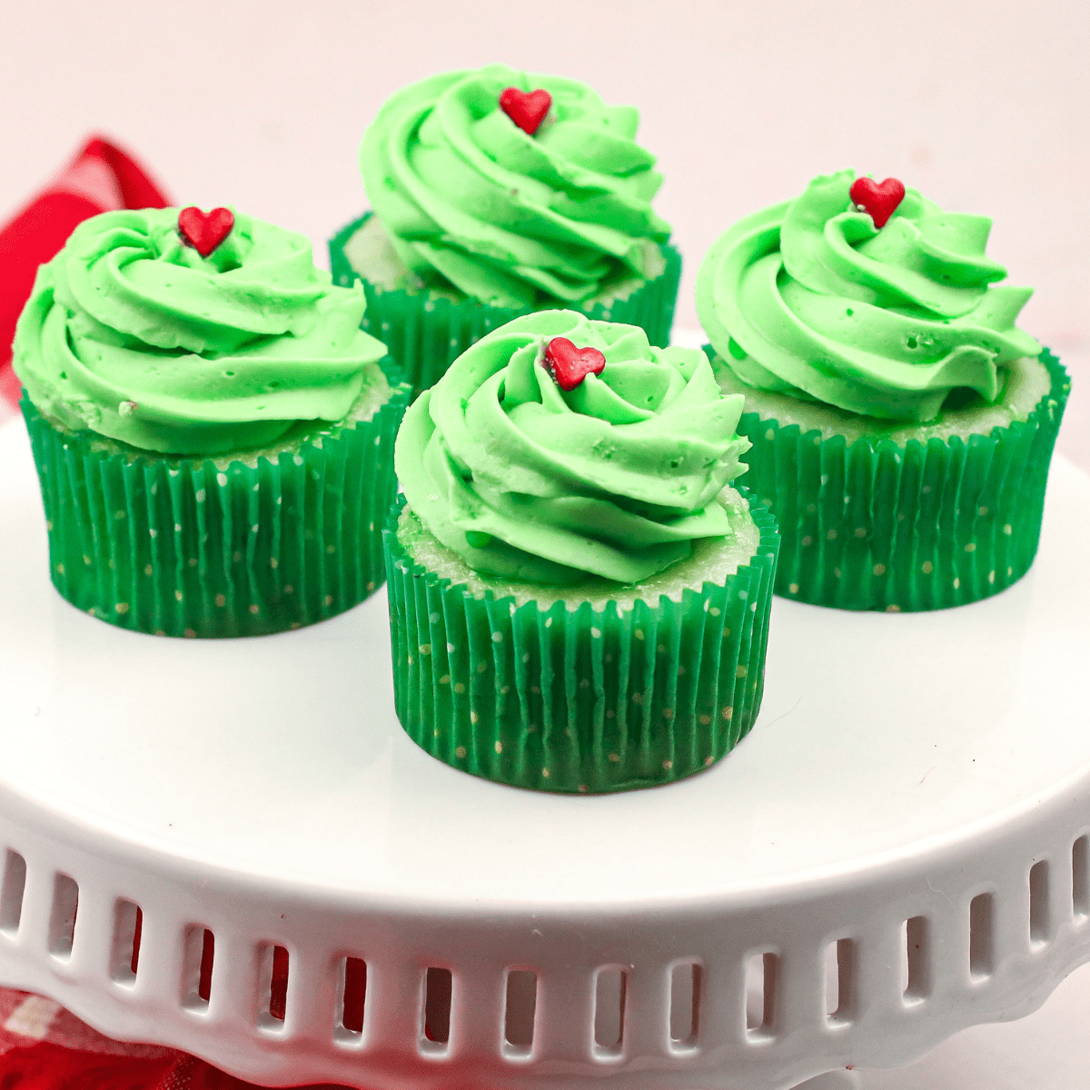 a close up of four green Grinch pistachio flavored cupcakes on a cake plate