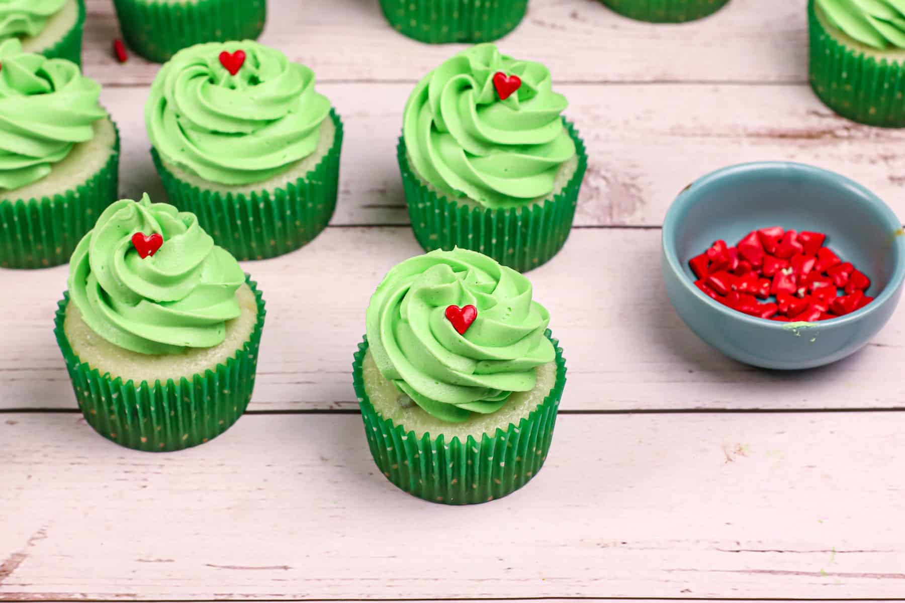 a bunch of Grinch cupcakes with green frosting and red candy hearts