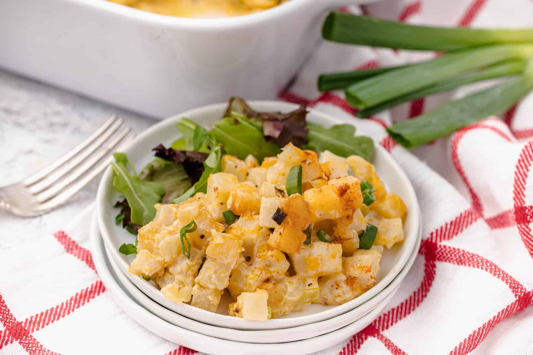 one serving of healthy hash brown casserole on a white plate with a small salad