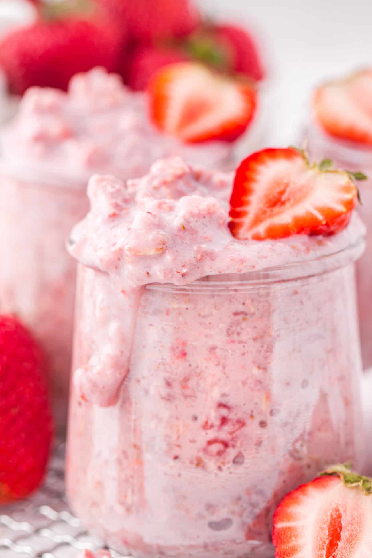 a small jar of strawberry overnight oats topped with half of a fresh strawberry with a drip running down the side