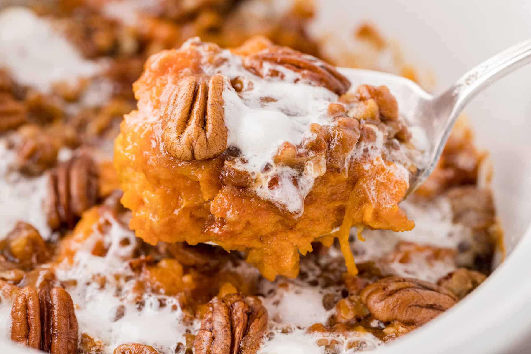 a close up of sweet potatoes made in the crockpot with marshmallows and pecans