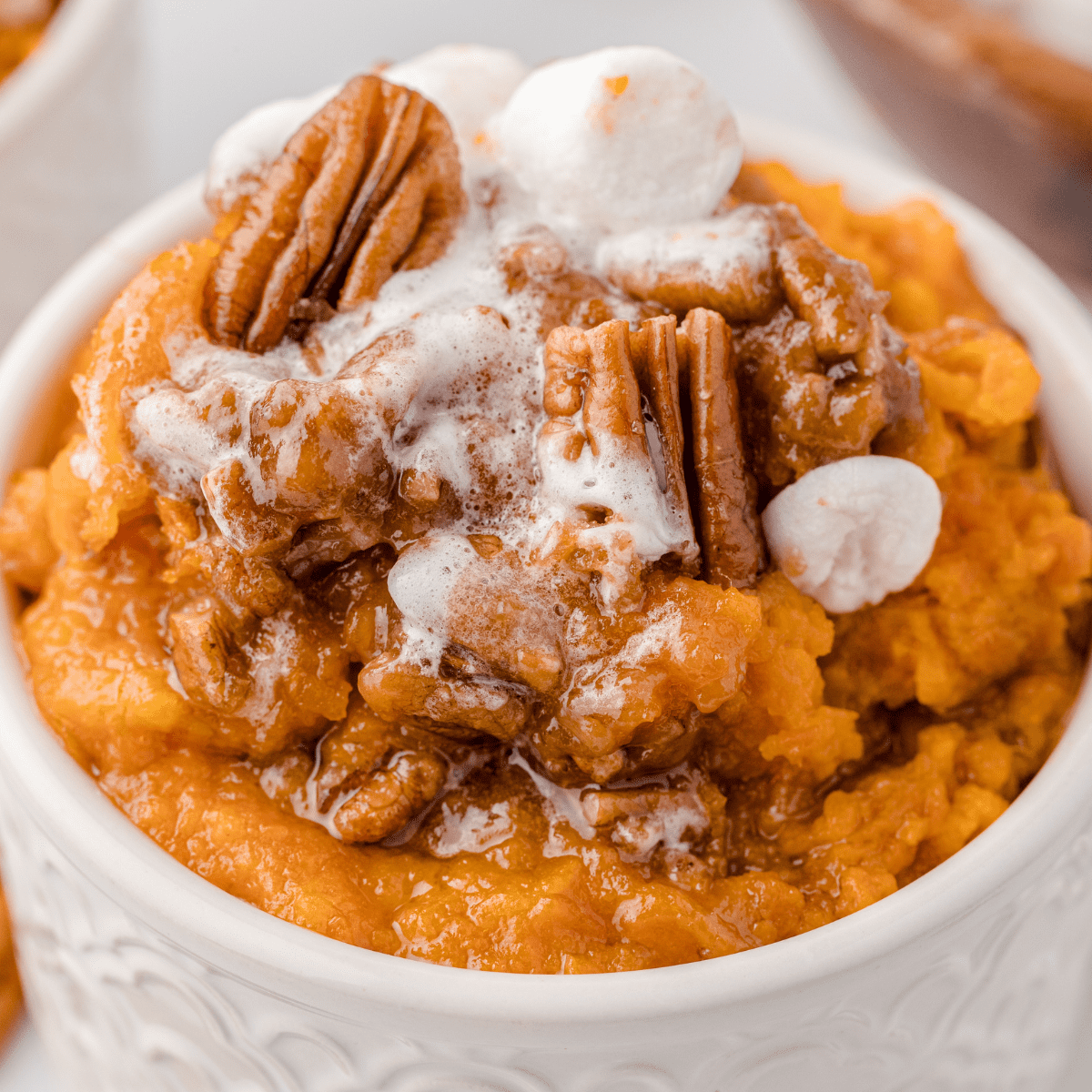 sweet potatoes topped with pecans and marshmallows in a white bowl