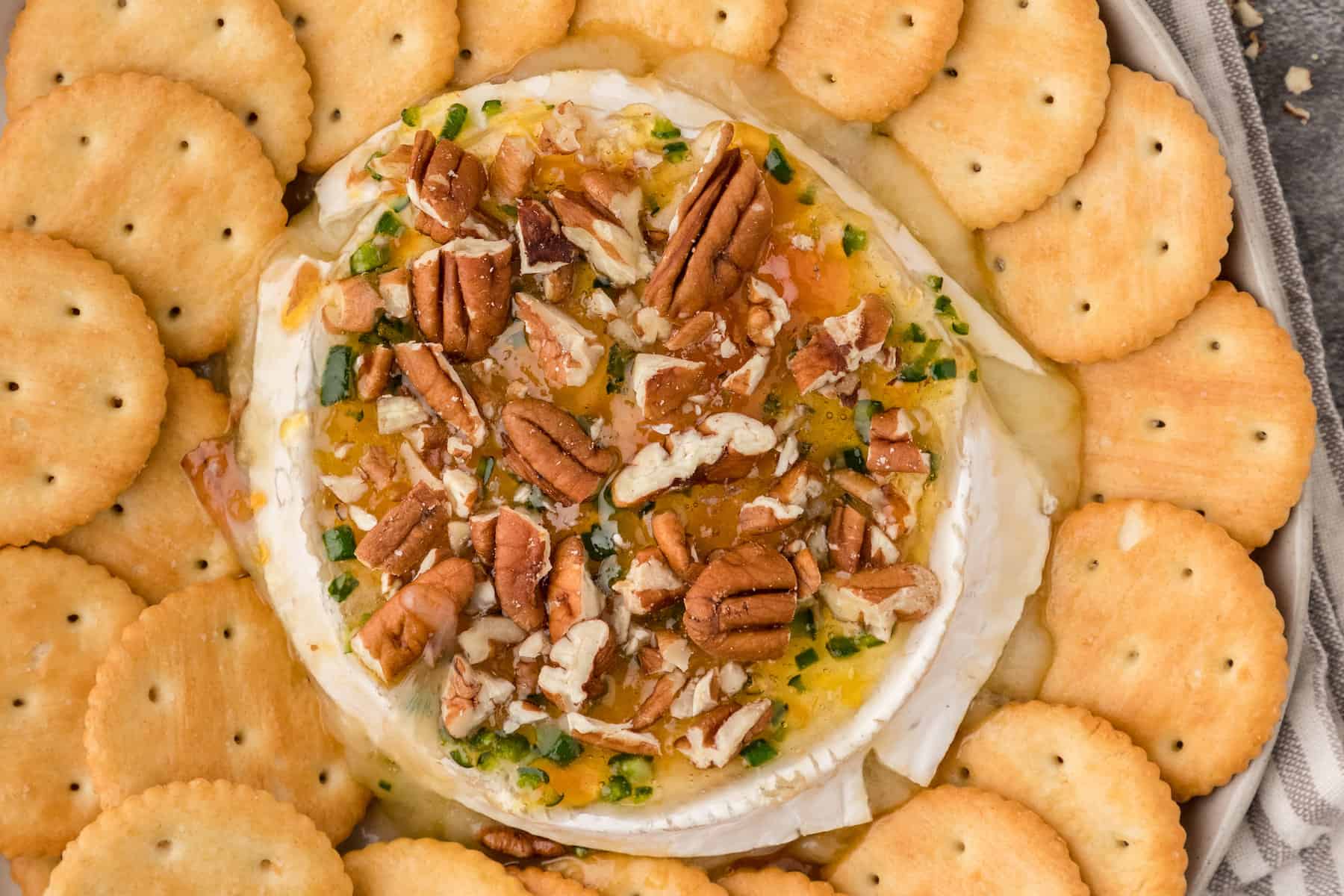 spicy baked brie with apricot jam, jalapeño peppers, and pecans surrounded by Ritz crackers