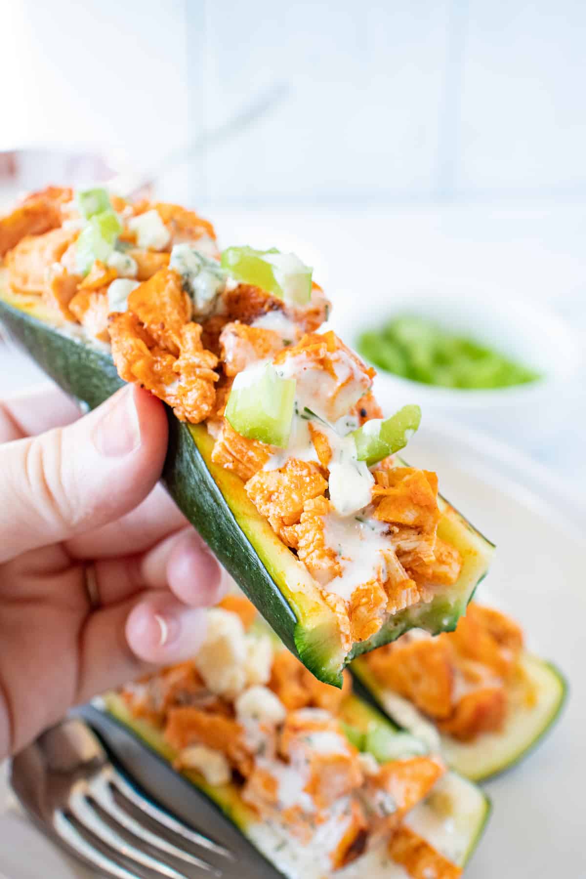 a hand holding a buffalo chicken zucchini boat