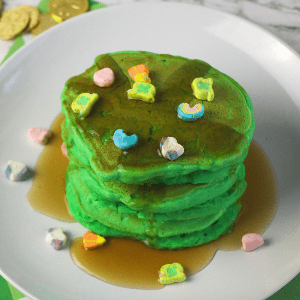 a stack of green pancakes with Lucky Charms surrounded by St. Patrick's Day gold coins
