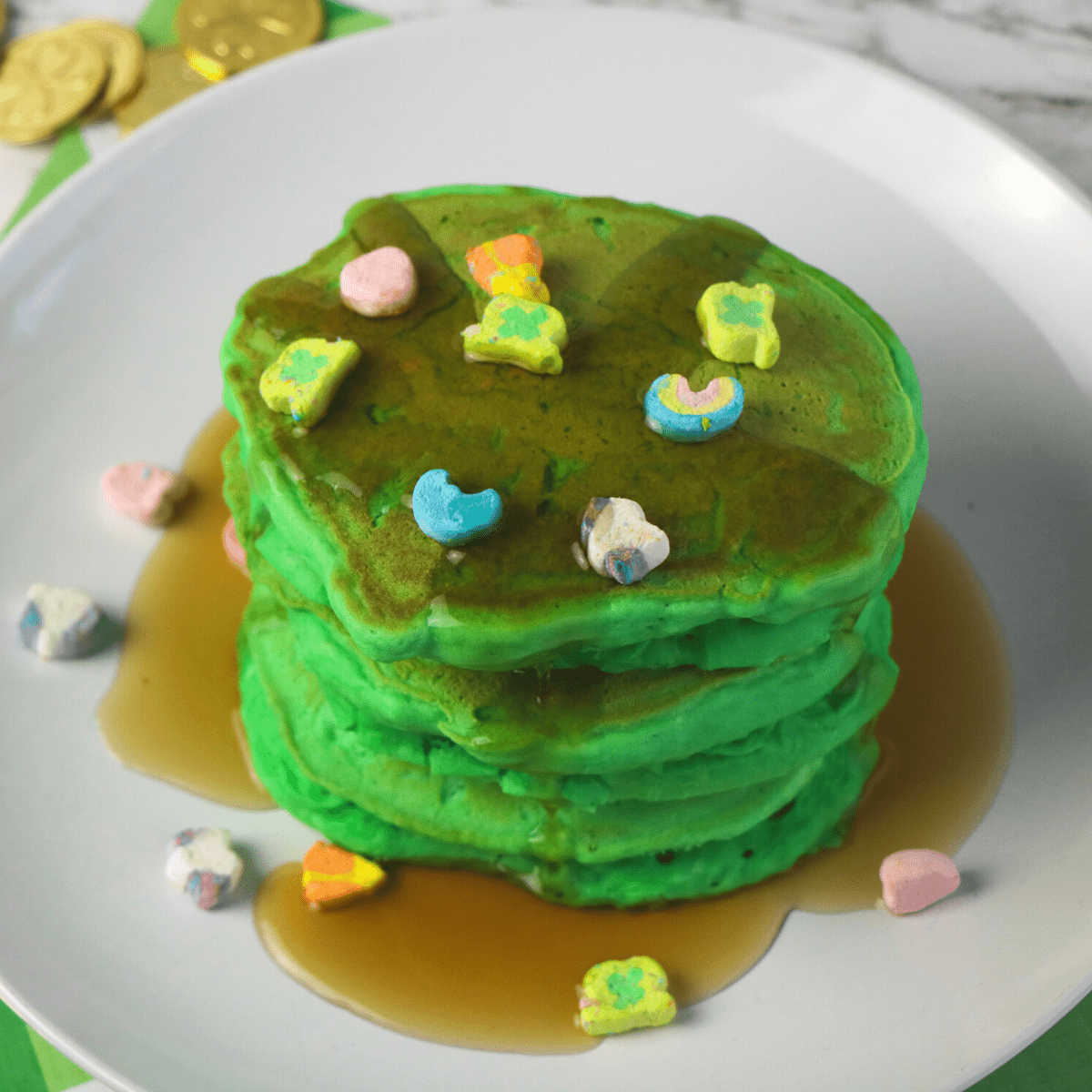 a stack of green pancakes with Lucky Charms surrounded by St. Patrick's Day gold coins