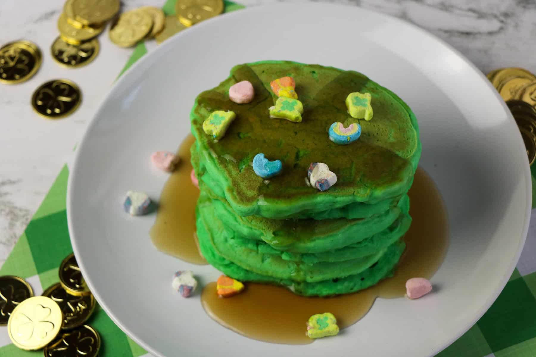 a stack of green pancakes with Lucky Charms surrounded by St. Patrick's Day gold coins