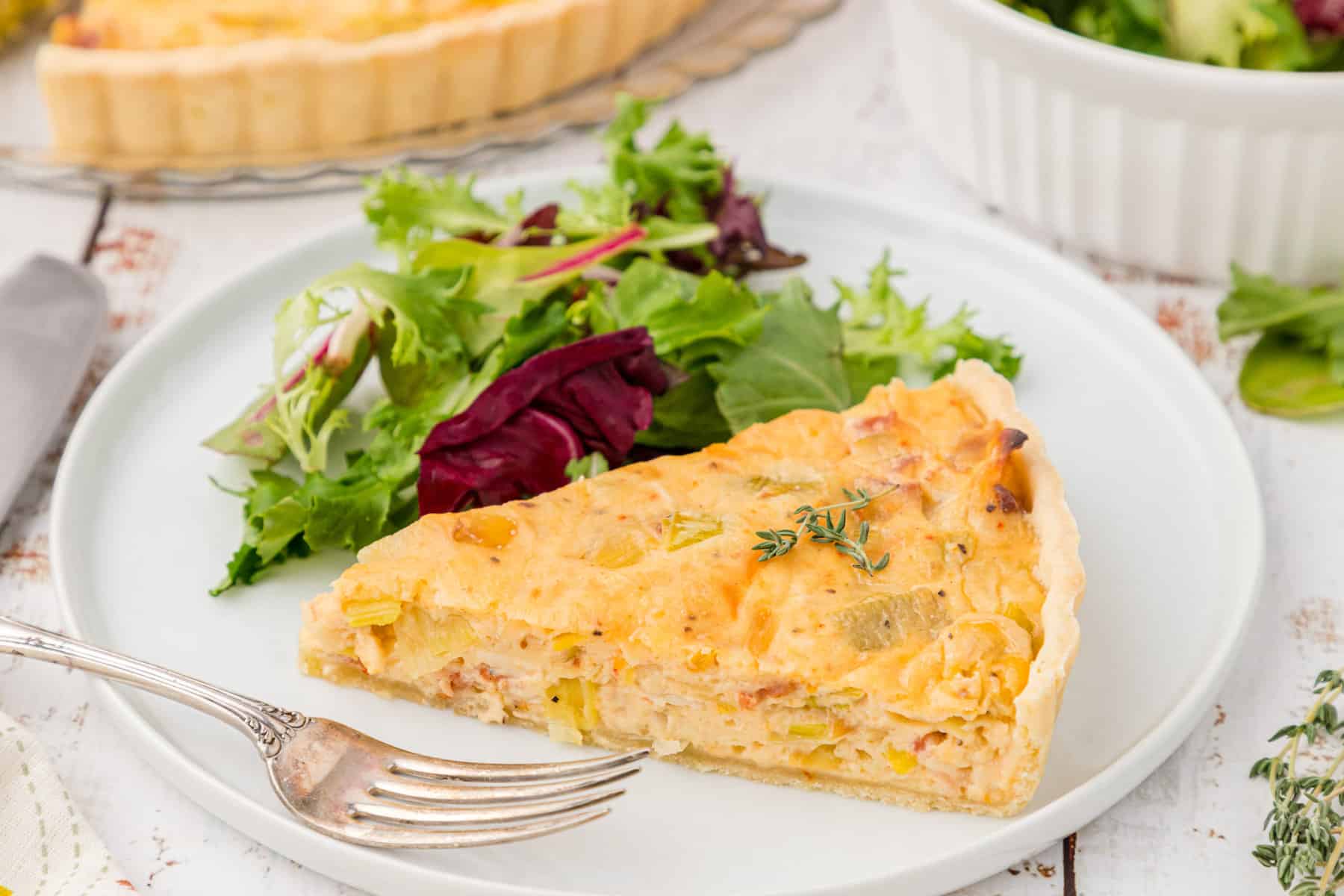 one slice of bacon leek tart with onions on a plate with a green salad