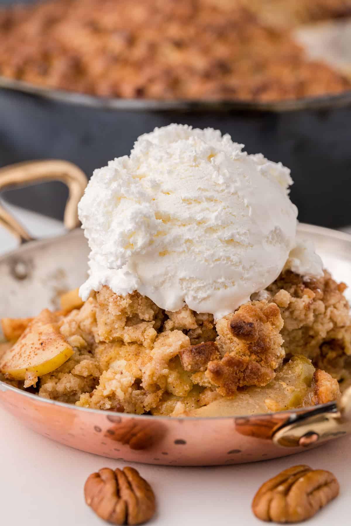 a copper bowl of apple crisp topped with ice cream