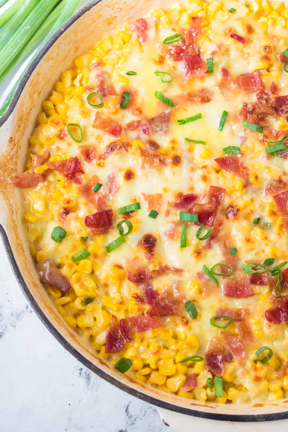 a close up of cheesy skillet corn with bacon in a skillet