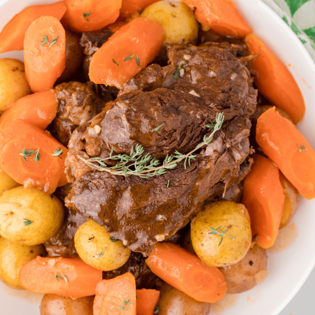 Chuck roast topped with homemade beef gravy with carrots and potatoes on a white platter