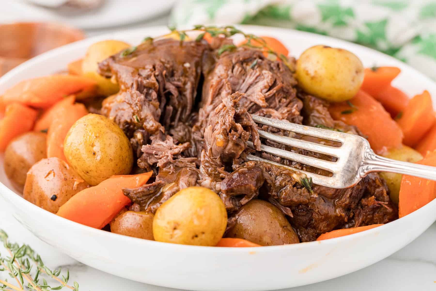 A close up of a single serving of chuck roast with carrots, potatoes, and homemade beef gravy on a small white plate