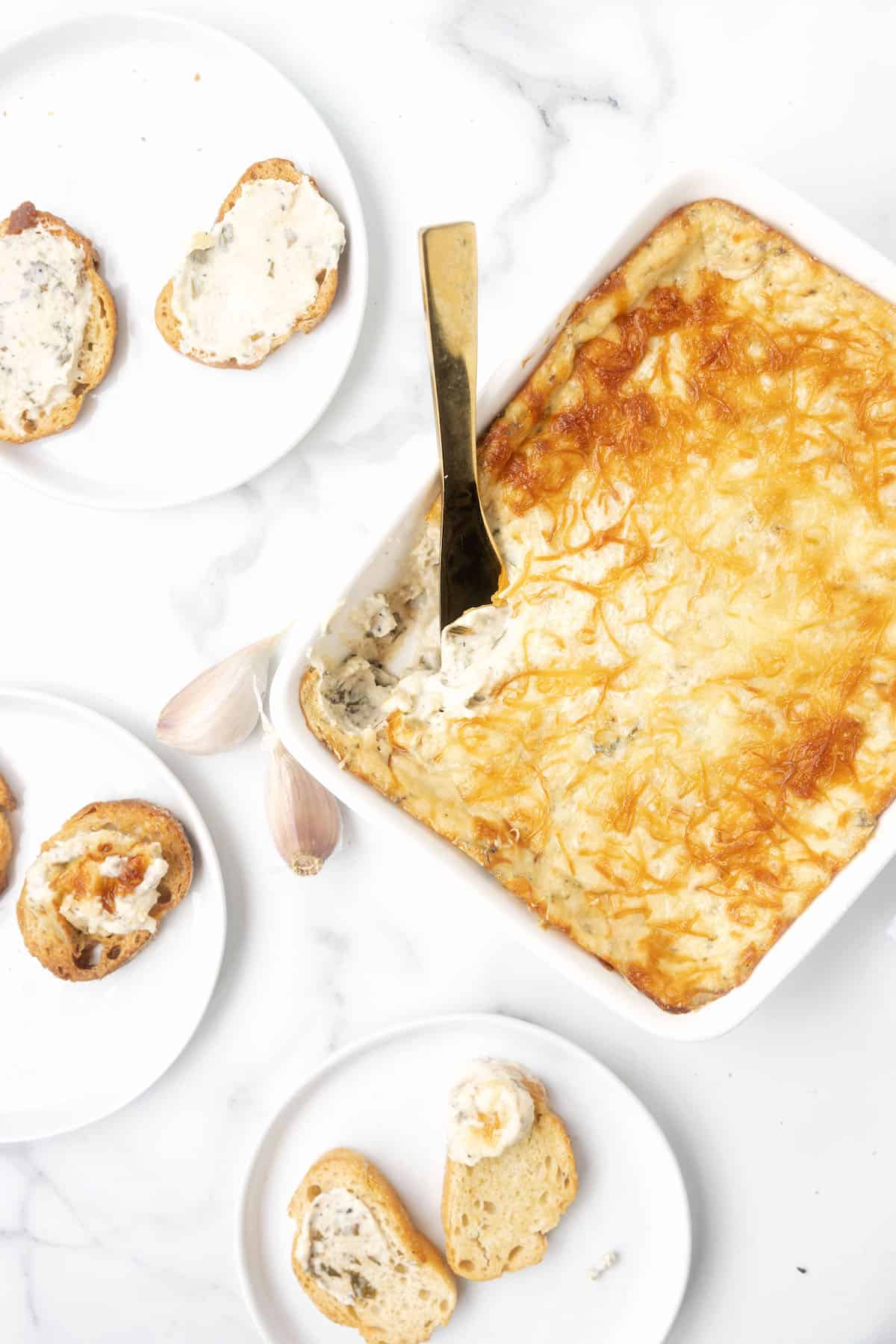 a baking dish with cheesy garlic bread dip and several plates with crostini