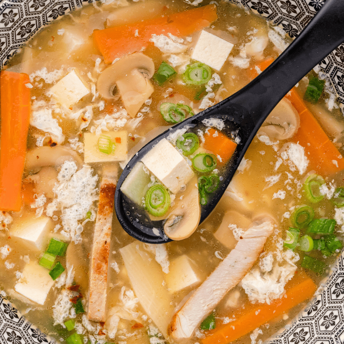 a close up of hot and sour soup in a blue and white bowl