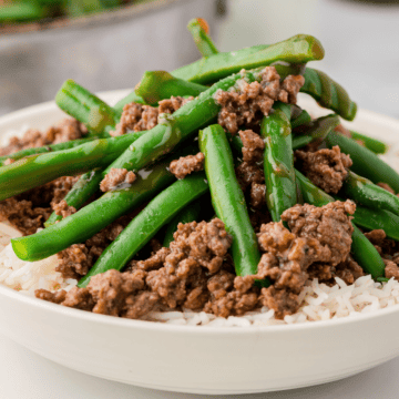 beef and green bean stir fry on top of rice in a white bowl
