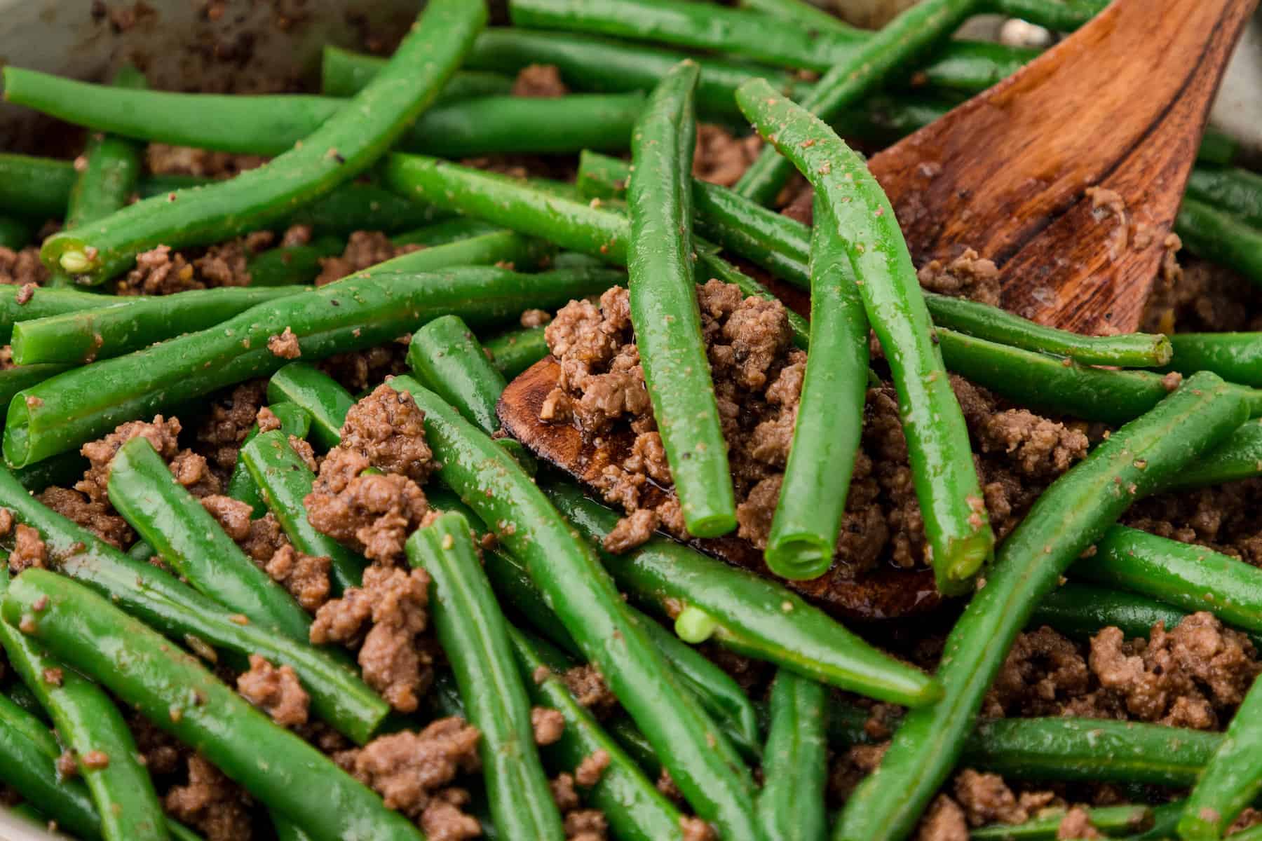 a close up of beef and green beans stir fry with a wooden spatula