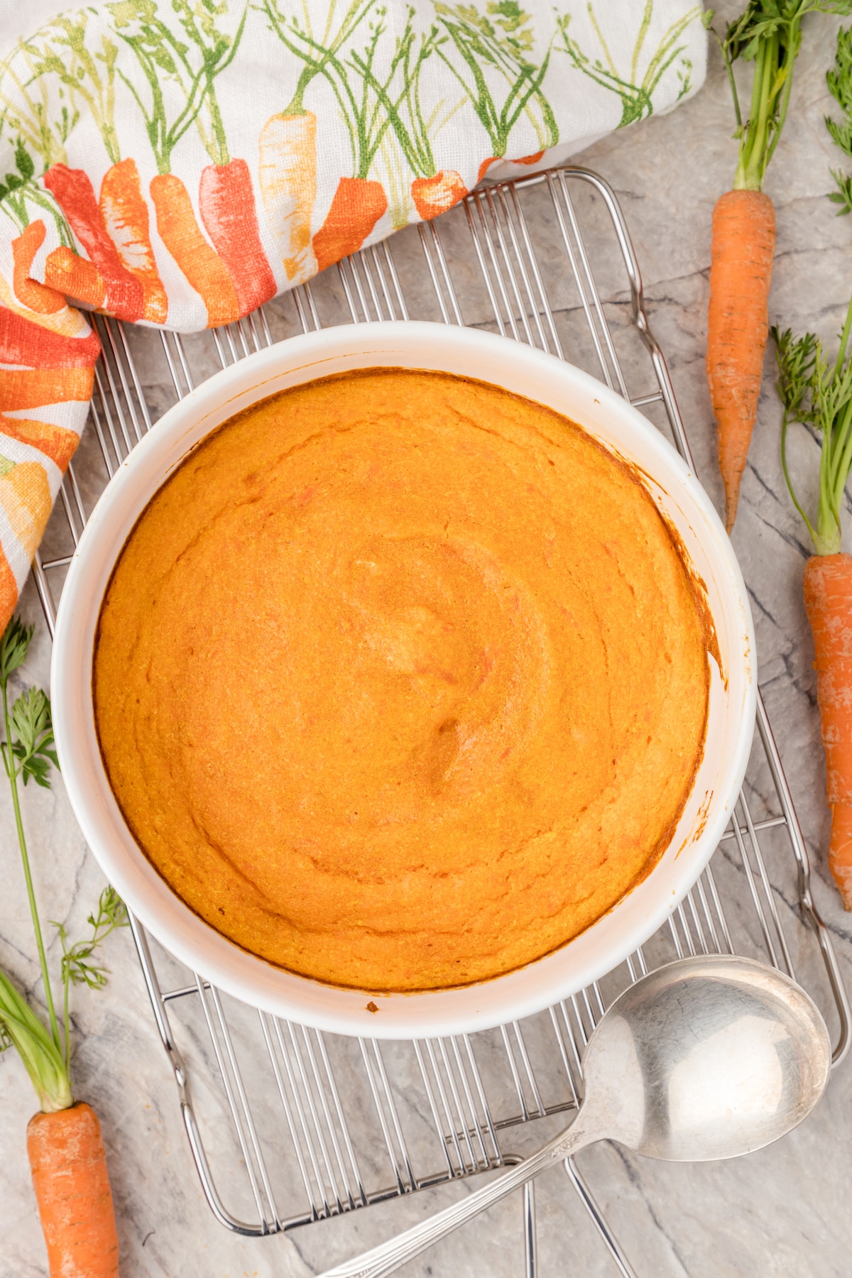 carrot souffle in a white baking dish with carrots around it