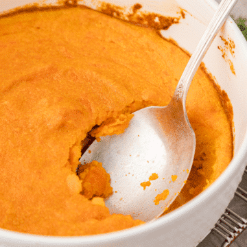 carrot souffle in a white baking dish with a large silver serving spoon