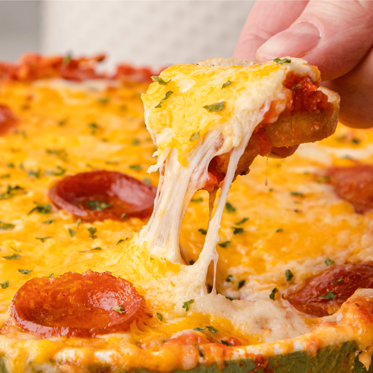 pepperoni pizza dip with crostini and strings of cheese hanging down