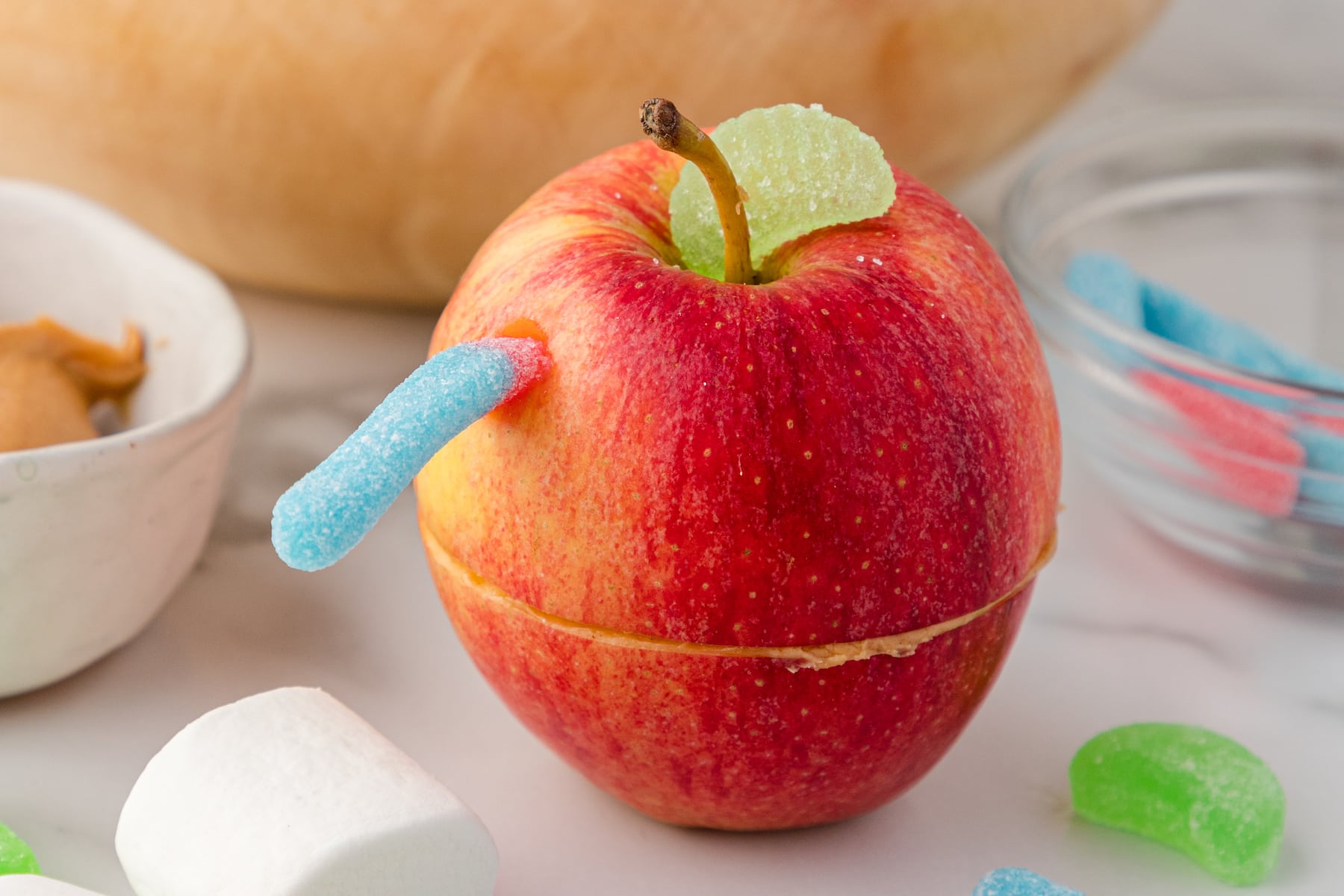 a close up of an apple snack for kids with a gummy worm and a spearmint leaf