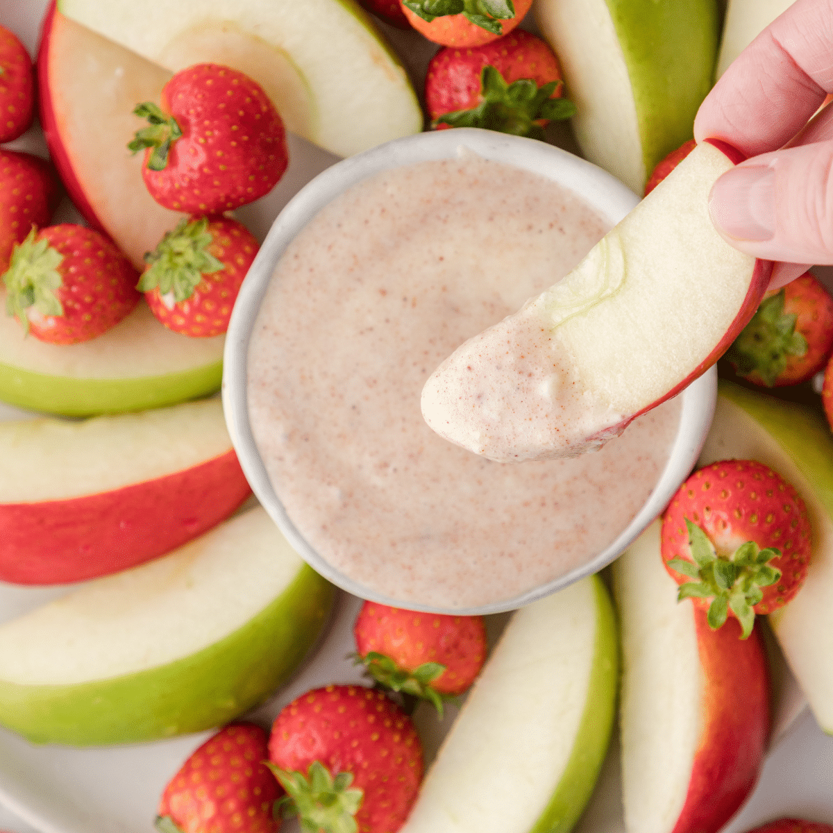 an apple dipped in cinnamon cream cheese fruit dip with apple slices and strawberries in the background