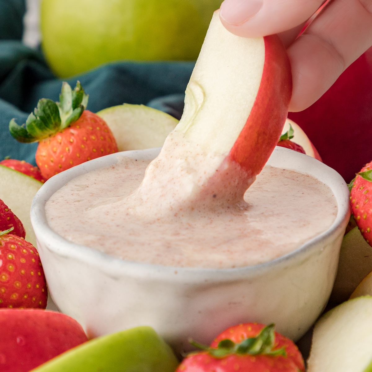 an apple dipping in cinnamon cream cheese fruit dip