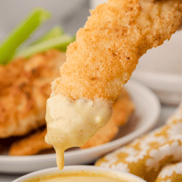 a close up of a gluten free chicken tender dripping with honey mustard sauce
