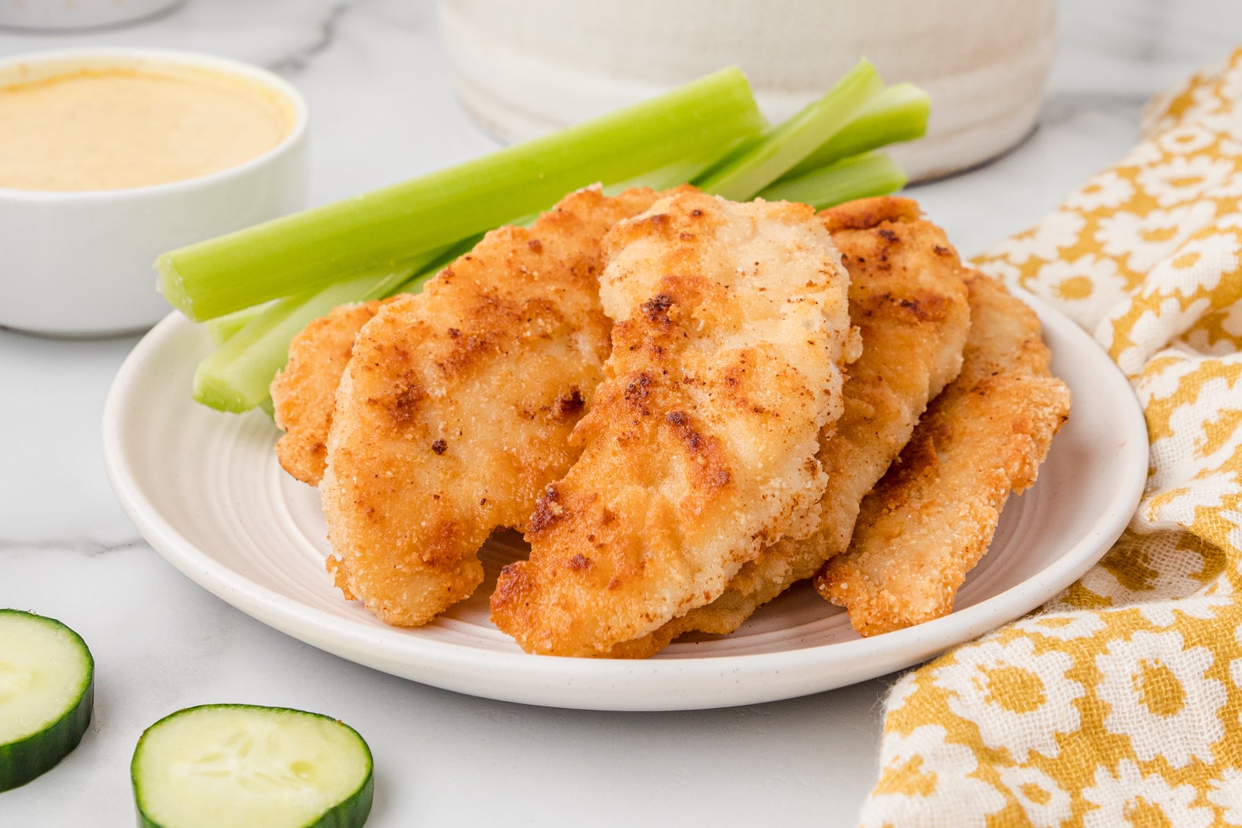 gluten free chicken tenders on a white plate with celery sticks and cucumber slices