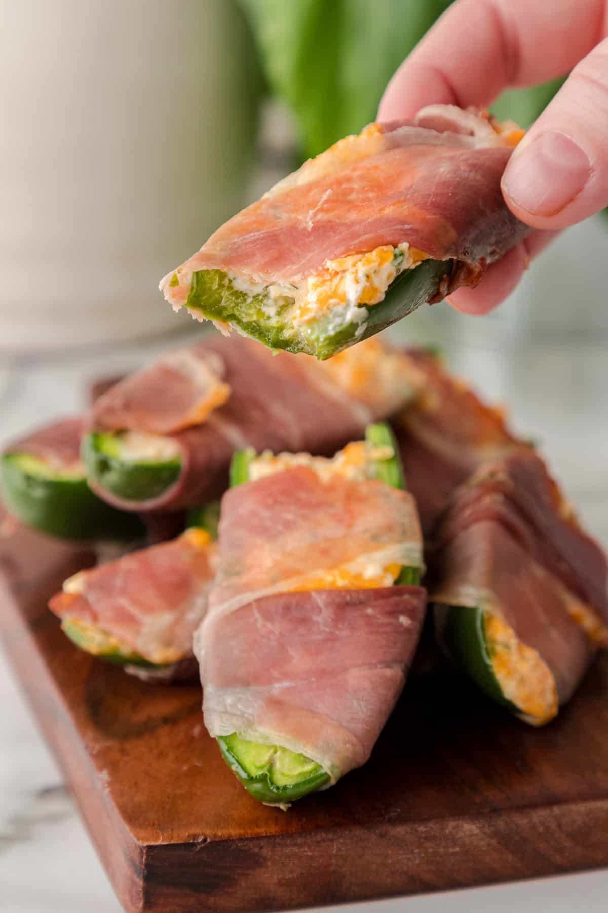 baked Low carb Keto Jalapeño Poppers with prosciutto on a cutting board with one popper bitten in half