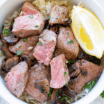 Air Fryer Steak Bites with Mushrooms in a white bowl with a lemon wedge
