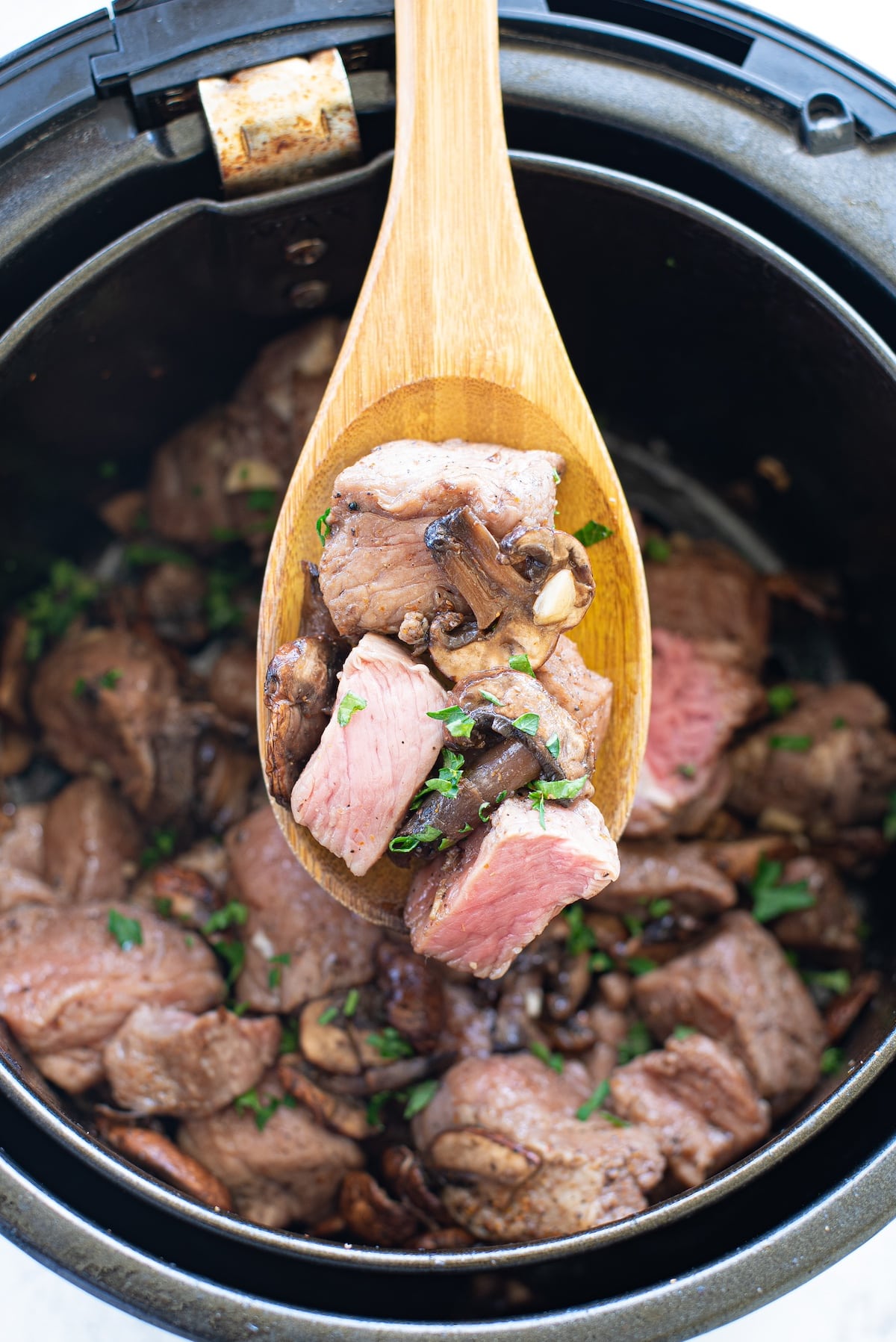 air fryer steak bites and mushrooms on a wooden spoon over top of the air fryer basket
