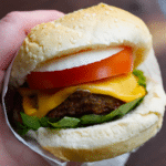a close up of an air fryer turkey burger with cheese, tomato, onion, and lettuce being held in a hand