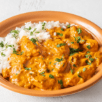 chicken tikka masala over rice on an orange plate