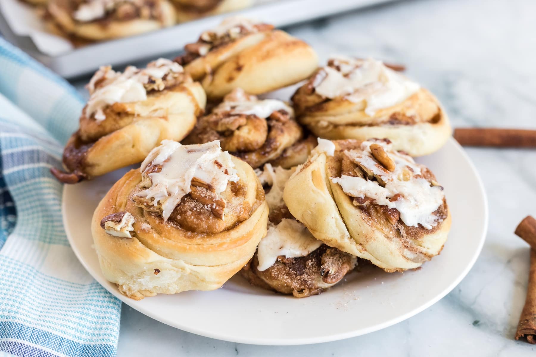a plate full of mini cinnamon rolls topped with cinnamon-sugar, chopped pecans, and homemade icing