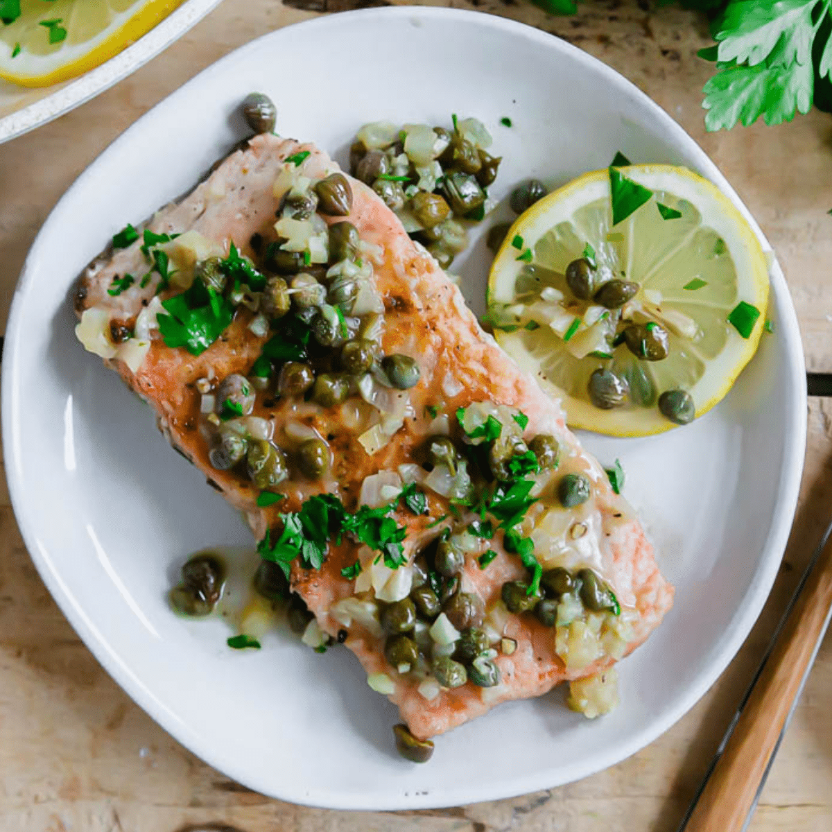 salmon piccata with shallots and capers on a white plate