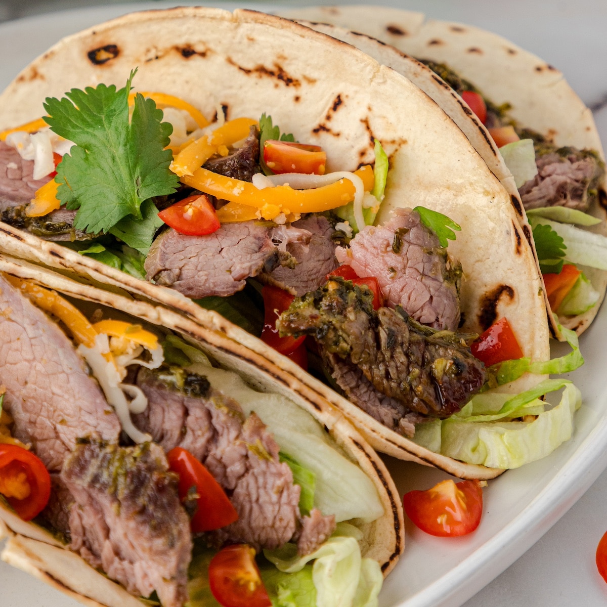 three marinated flank steak tacos with cilantro, tomatoes, cheese, and lettuce