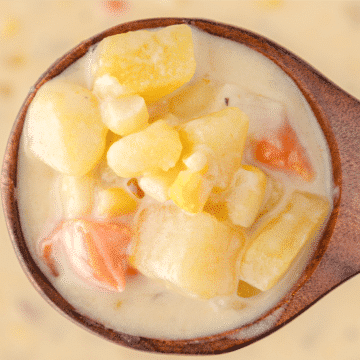 a ladle full of crockpot potato soup with potatoes, corn, and carrots