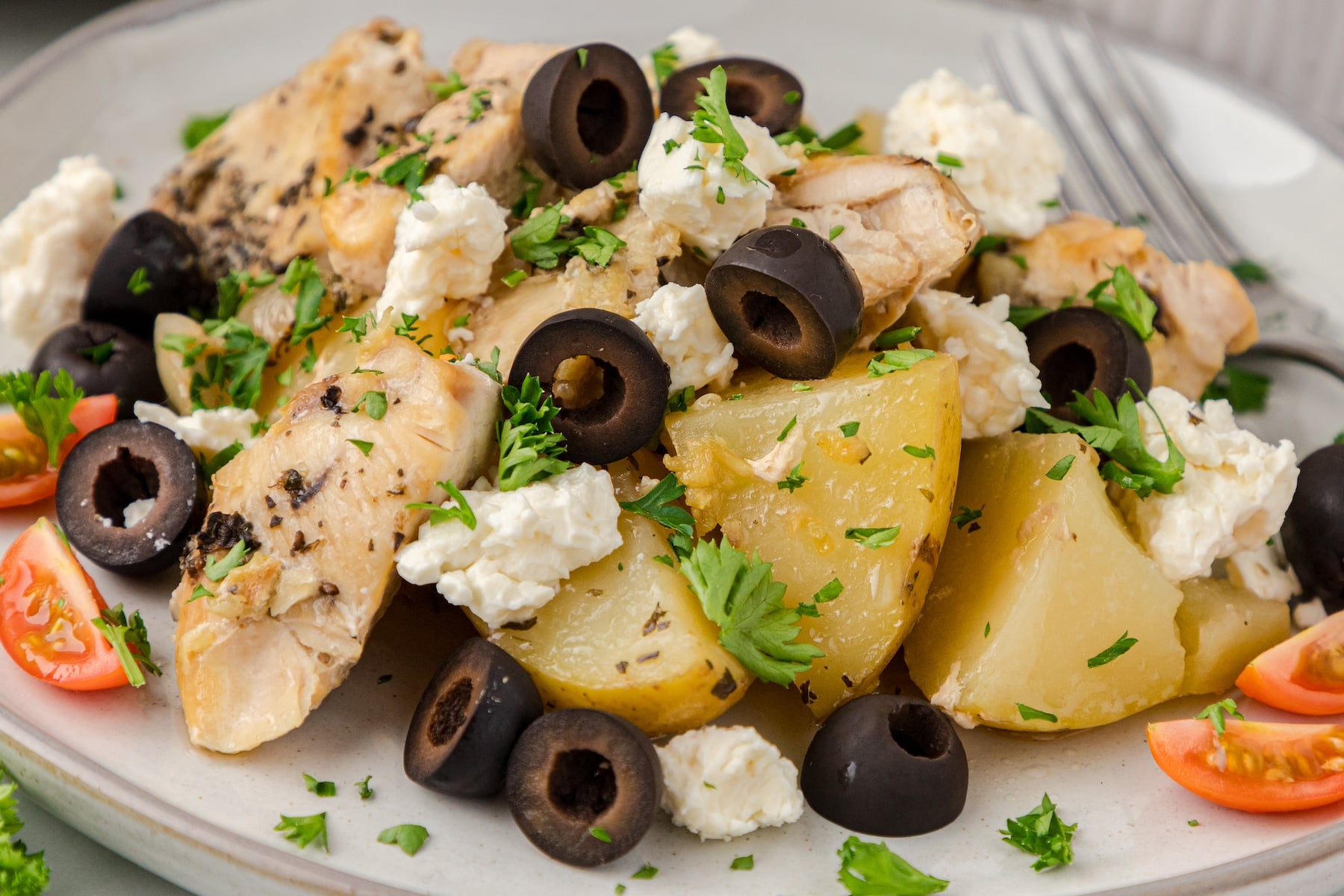 a close up of CrockPot Mediterranean chicken and potatoes topped with sliced black olives and crumbled feta cheese