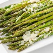 Garlic Roasted Asparagus with melted Parmesan cheese on a white plate