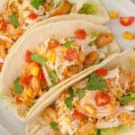three tacos made using Instant Pot chicken shredded and topped with rice, cheese, cilantro, beans, and tomatoes
