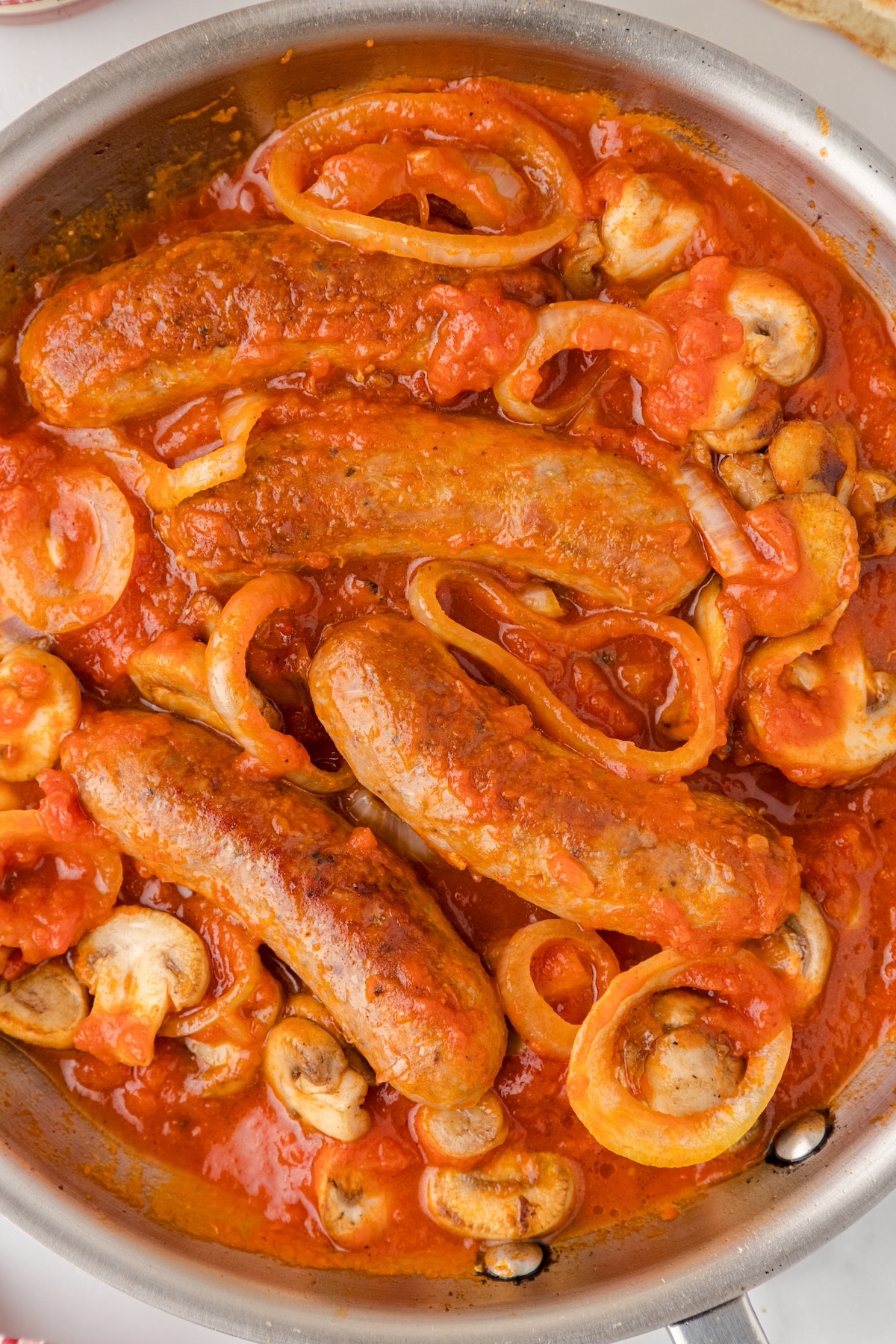 Italian sausages in a skillet with onions, mushrooms, and spaghetti sauce