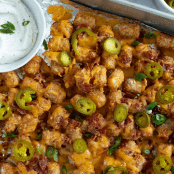 loaded tater tot nachos on a baking sheet with cheese, bacon, and jalapenos