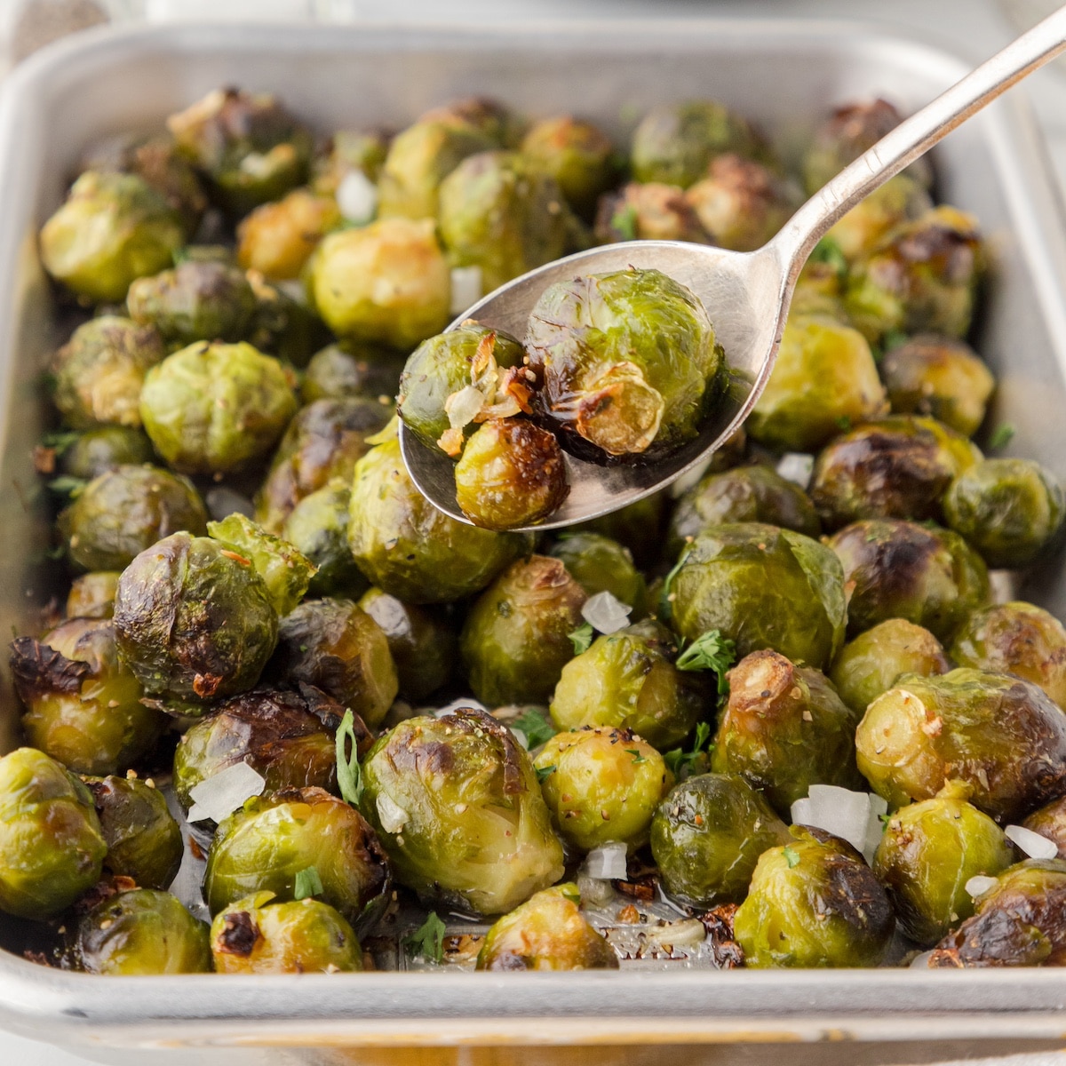 a serving spoon with three roasted brussels sprouts that were cooked from frozen over top of a sheet pan of roasted brussels sprouts