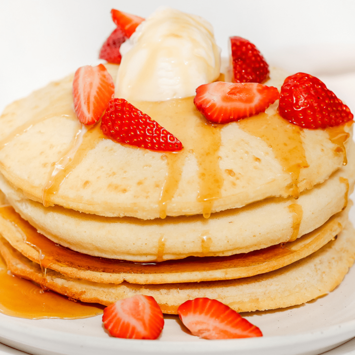 a close up of a stack of air fryer pancakes topped with strawberries, ice cream, and maple syrup