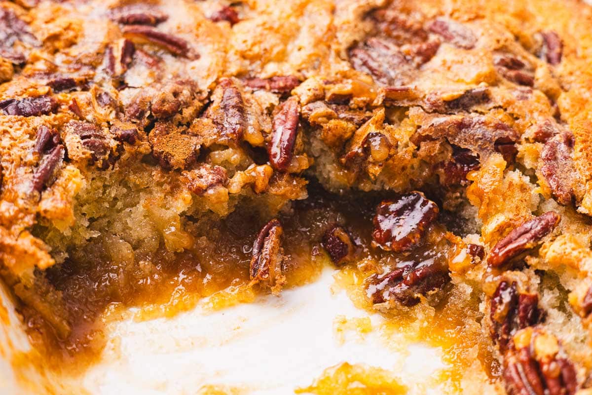 a close up of pecan pie cobbler with one piece cut out, showing the gooey filling