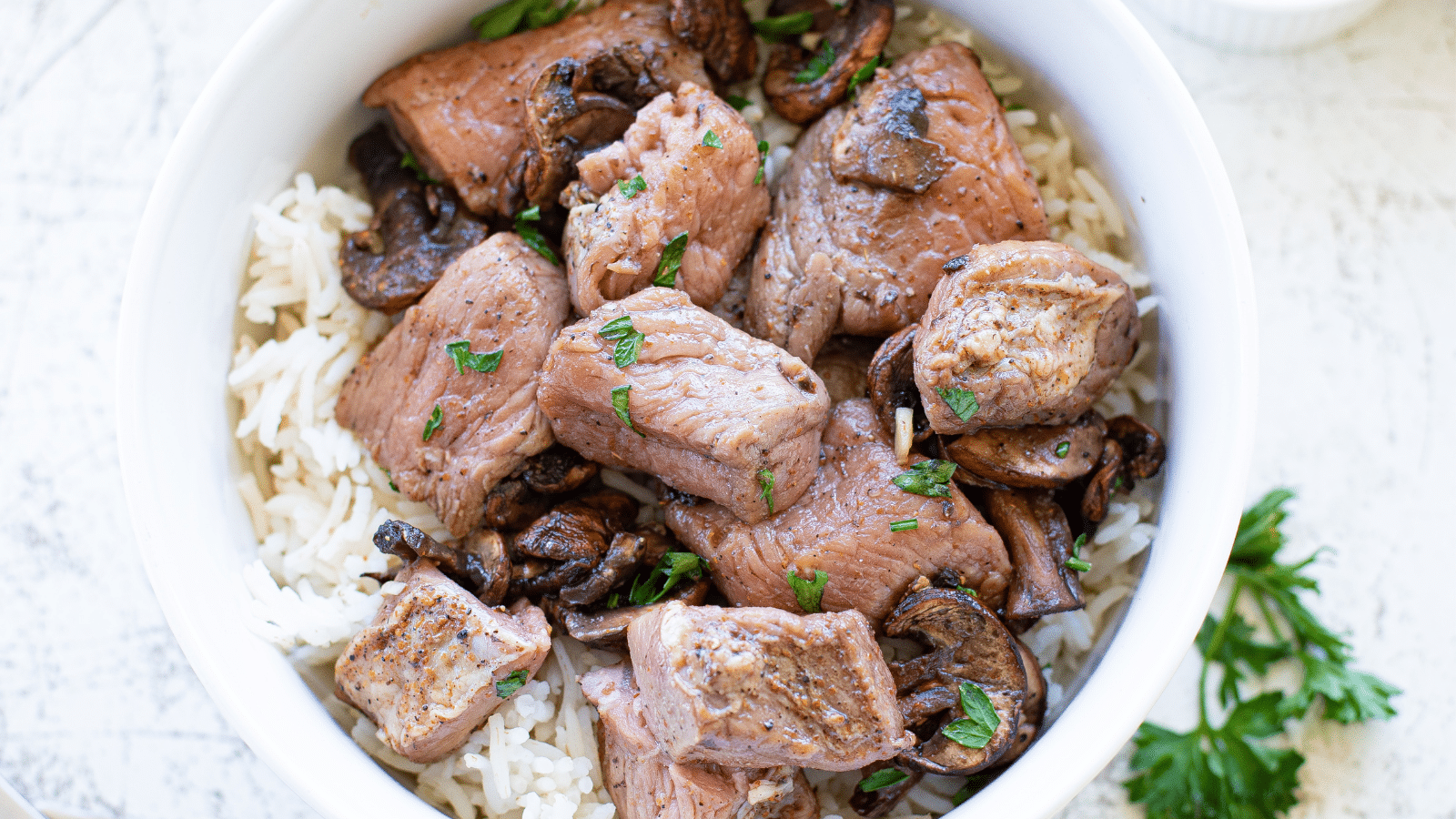 a close up of Air Fryer Steak Bites with Mushrooms over rice in a white bowl