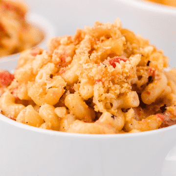 a close up of mac and cheese with tomatoes and breadcrumbs in a white bowl