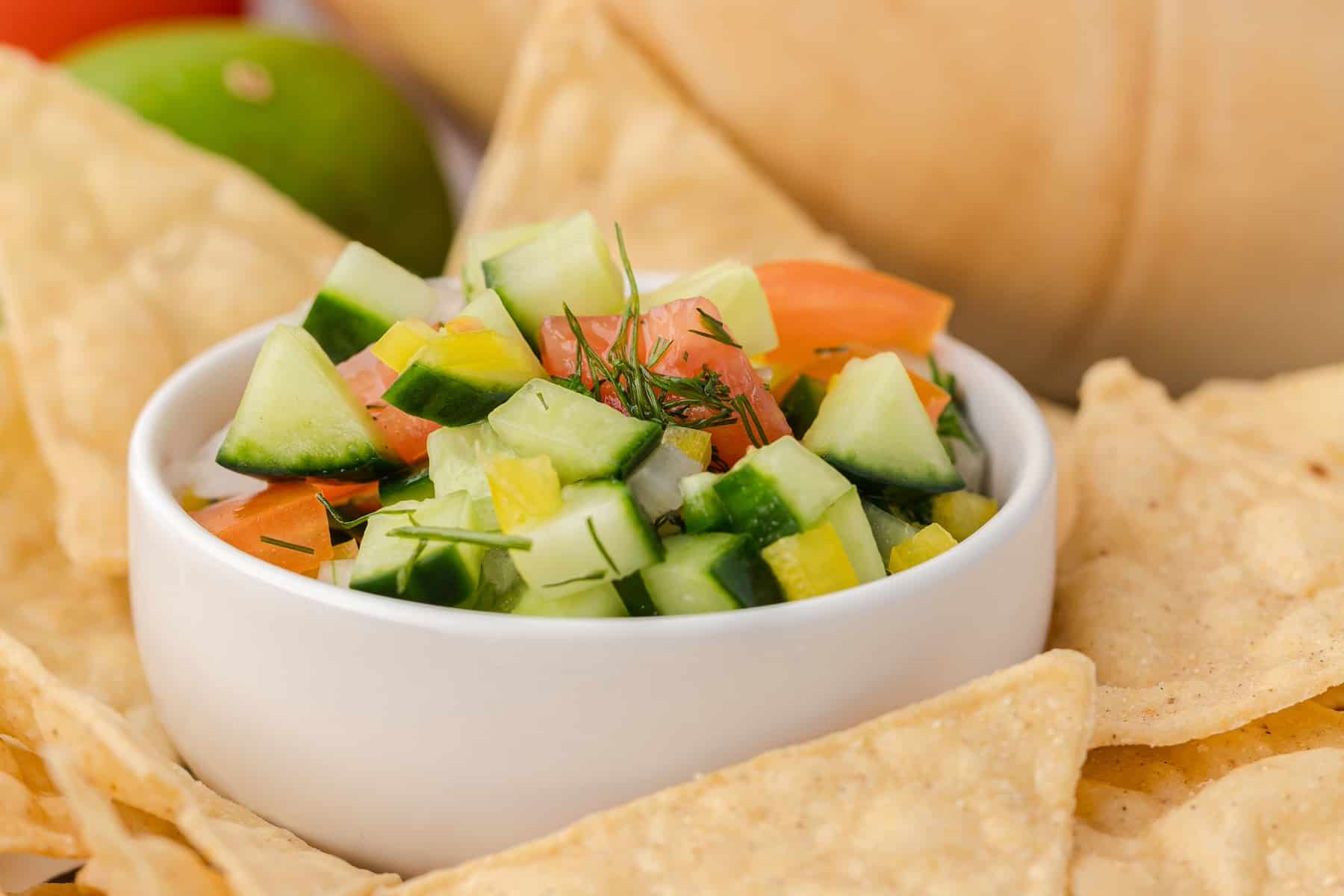cucumber salsa in a small white bowl surrounded by tortilla chips